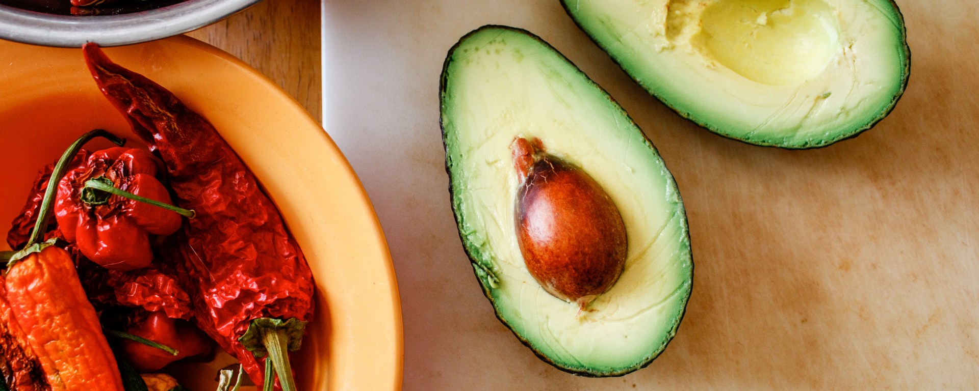 Peppers and an avocado sit on a table, ready for cooking